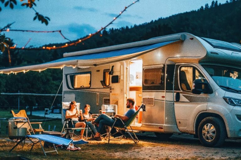 Eine Gruppe von Freunden sitzt in der Abenddämmerung an ihrem Wohnmobil und surft auf einem Laptop im Internet.