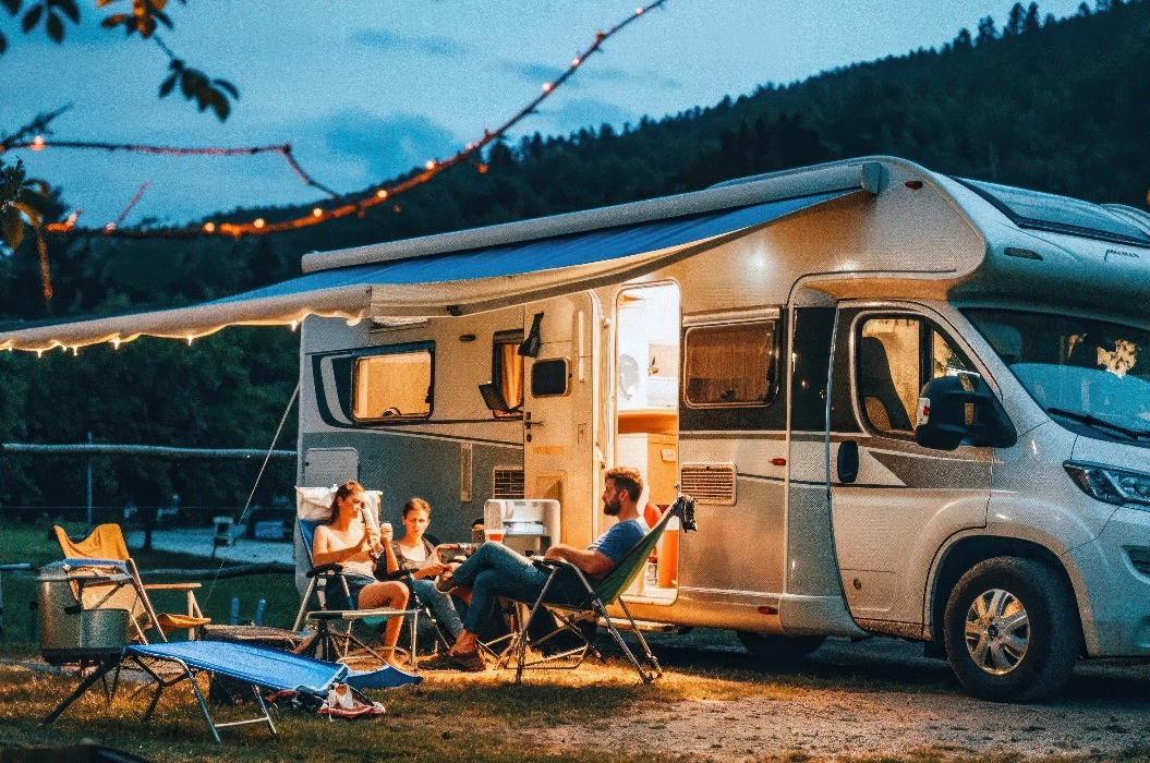 Eine Gruppe von Freunden sitzt in der Abenddämmerung an ihrem Wohnmobil und surft auf einem Laptop im Internet.