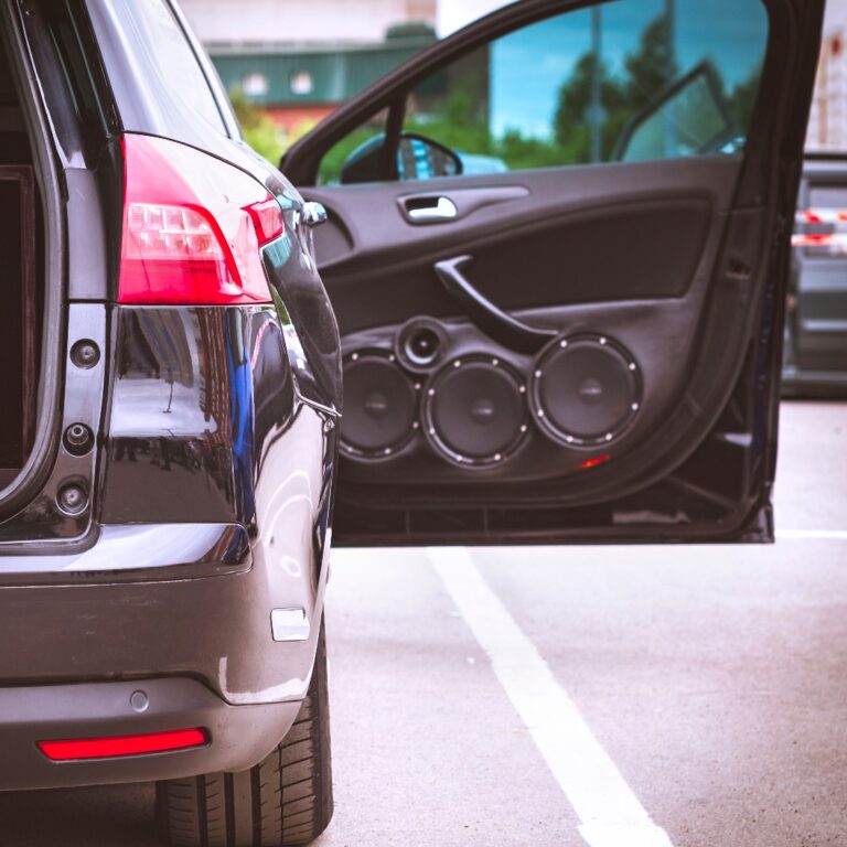 Rückansicht eines Autos mit geöffnetem Kofferraum und geöffneter Vordertür, ausgestattet mit einer eingebauten Car-Audio-Anlage, Lautsprechern und einem riesigen Subwoofer.